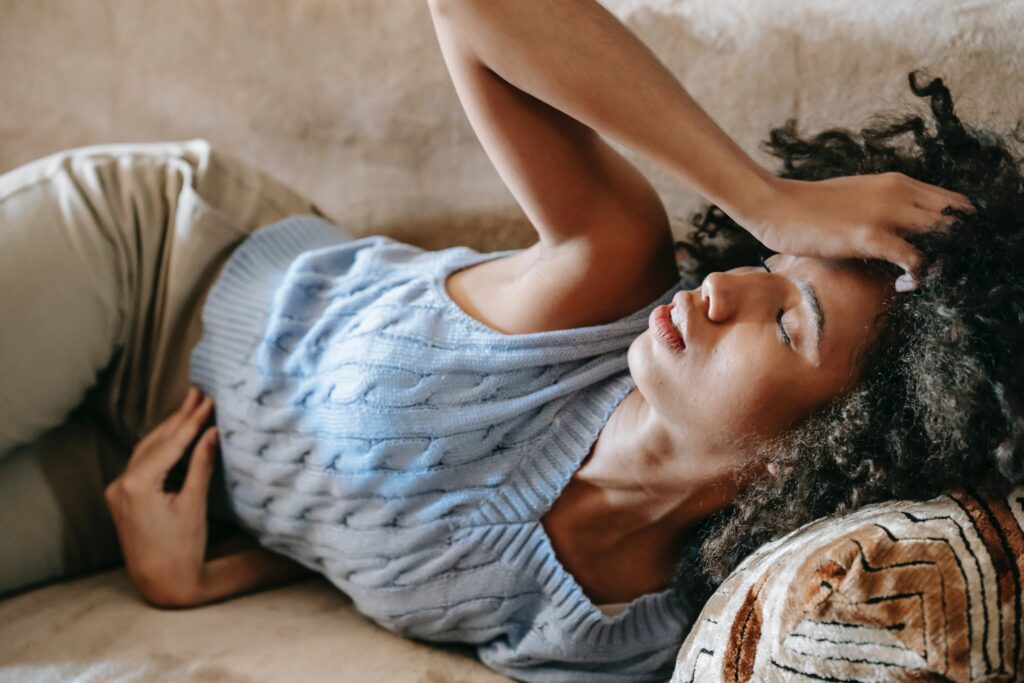 Woman laying down clutching her head and stomach feeling sore from stress and anxiety